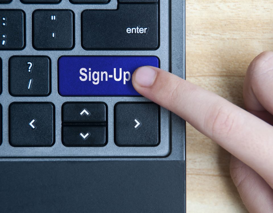Top view of hand pressing sign-up button on laptop keyboard.